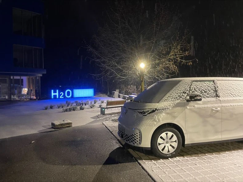 Photo d'un véhicule de service électrique devant un logo H2O lumineux sur un parking