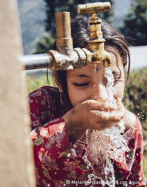 A Nepalese girl drinks clear water from a water pump